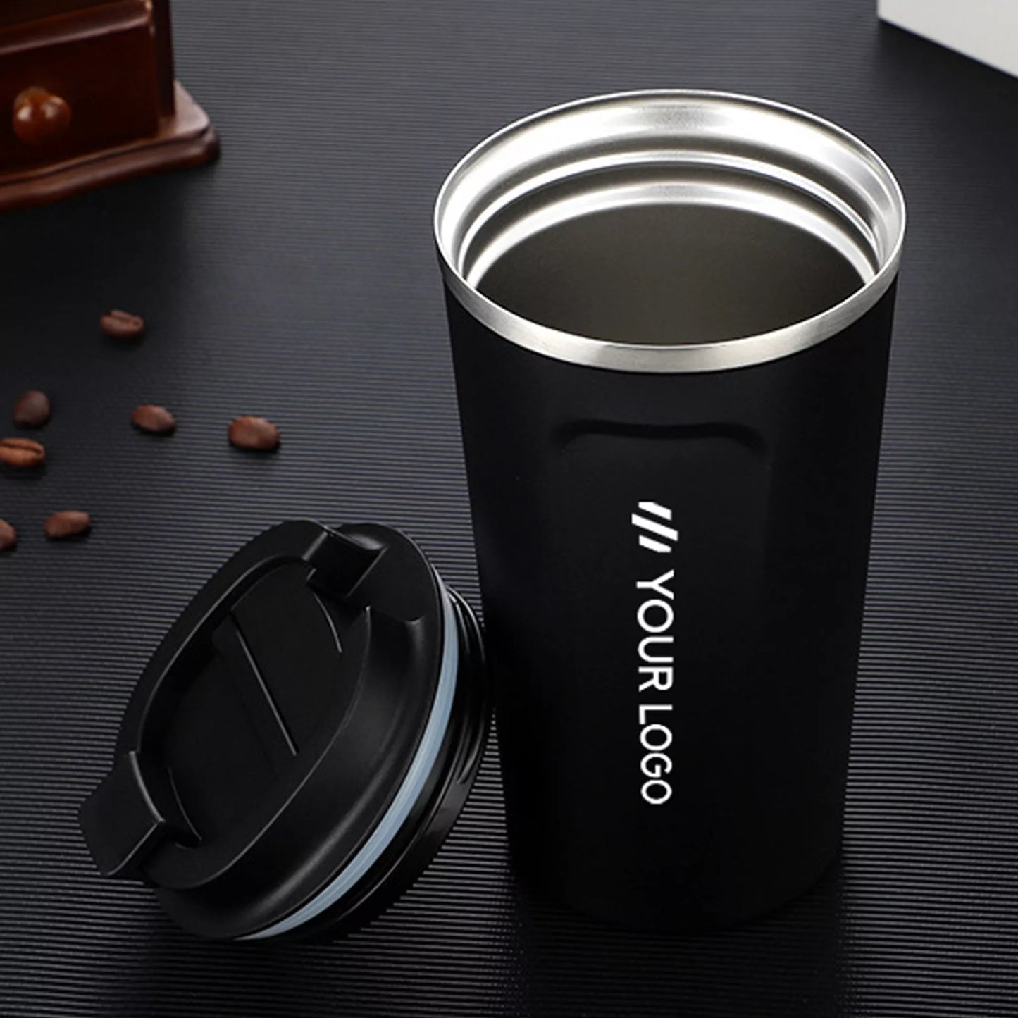 Black insulated tumbler with silver rim on a dark surface with coffee beans.