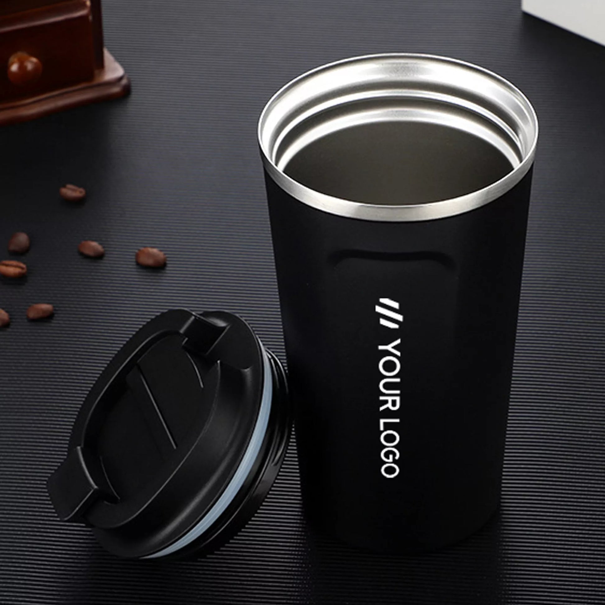 Black insulated tumbler with silver rim on a dark surface with coffee beans.